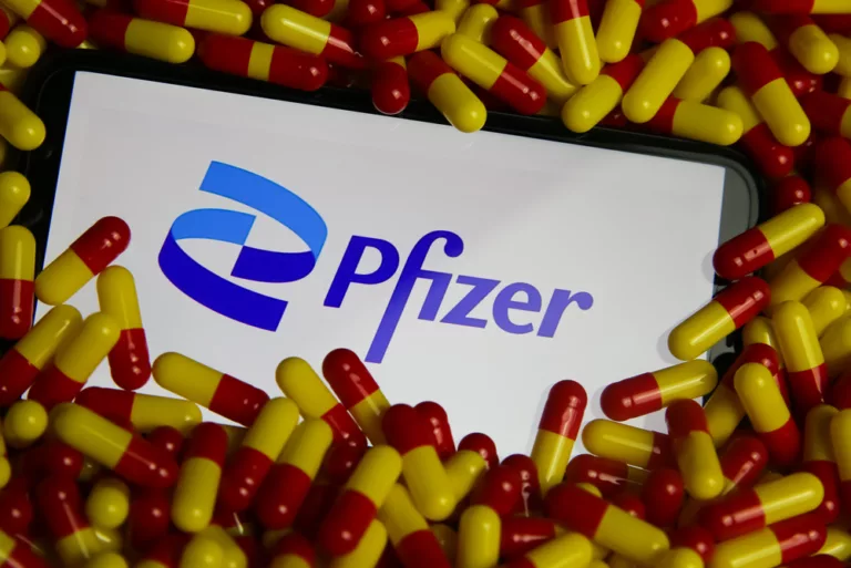 Nahaufnahme eines Handybildschirms mit Logo-Schriftzug des Pharmaunternehmens Pfizer in einem Pillenstapel